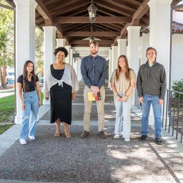 Science students posing with mentor in outdoor hallway