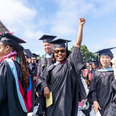 A graduate holding up her hand smiling in a group of graduates