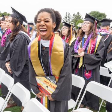 A graduating student yelling while holding a hat that says Black Native